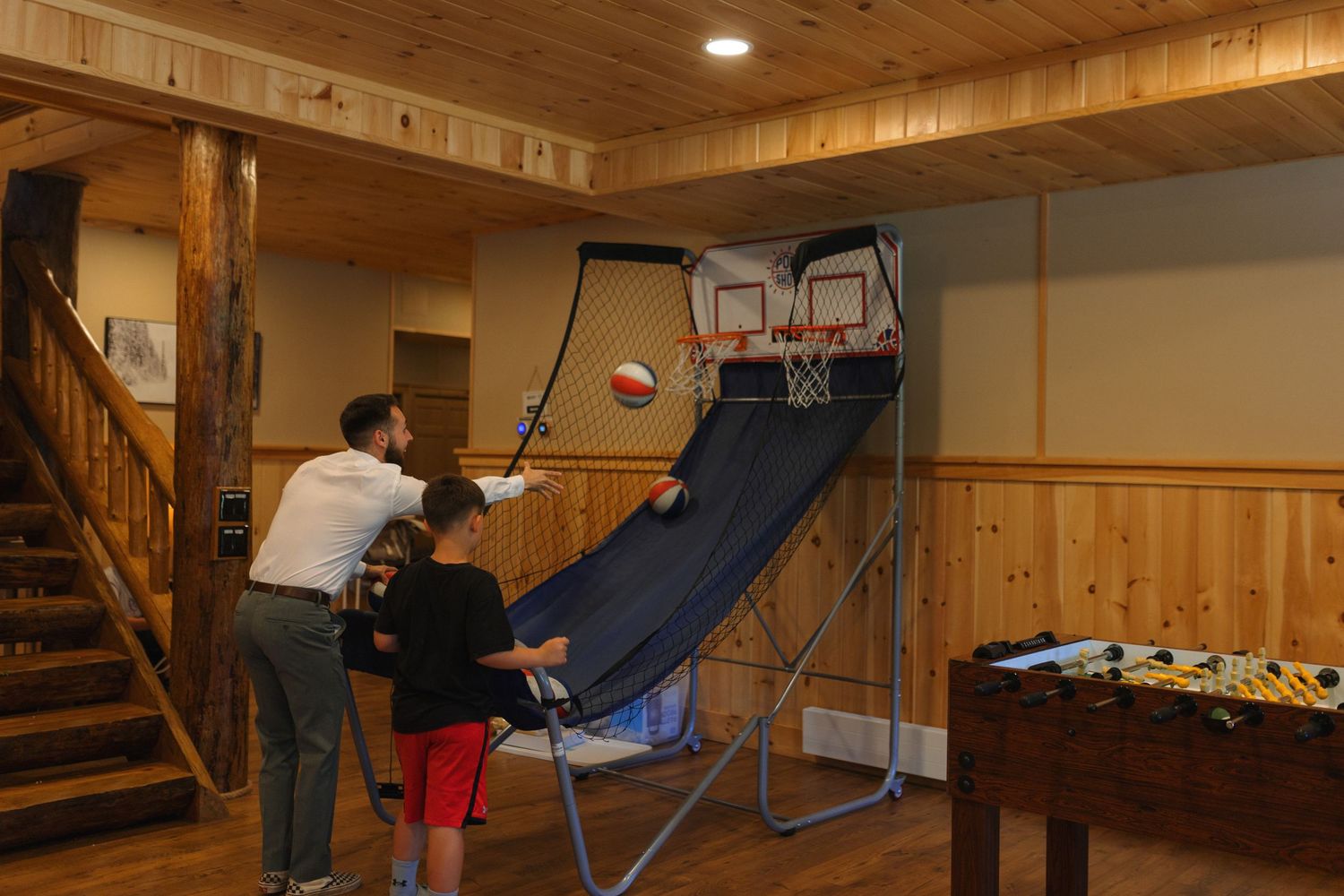 People playing indoor basketball on an arcade-style game in a wooden cabin recreation room.