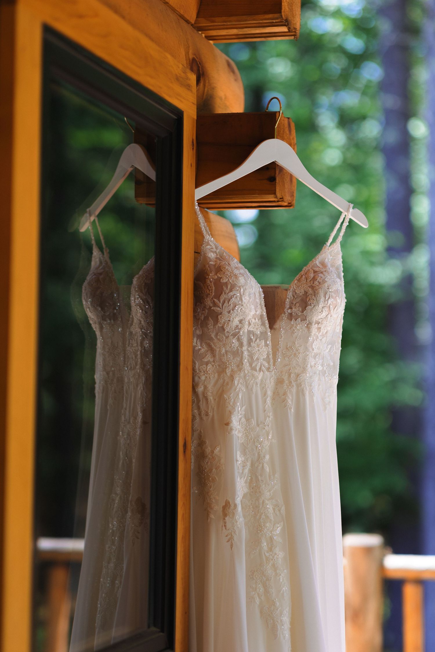 Elegant lace wedding dress hanging on wooden balcony with forest backdrop.