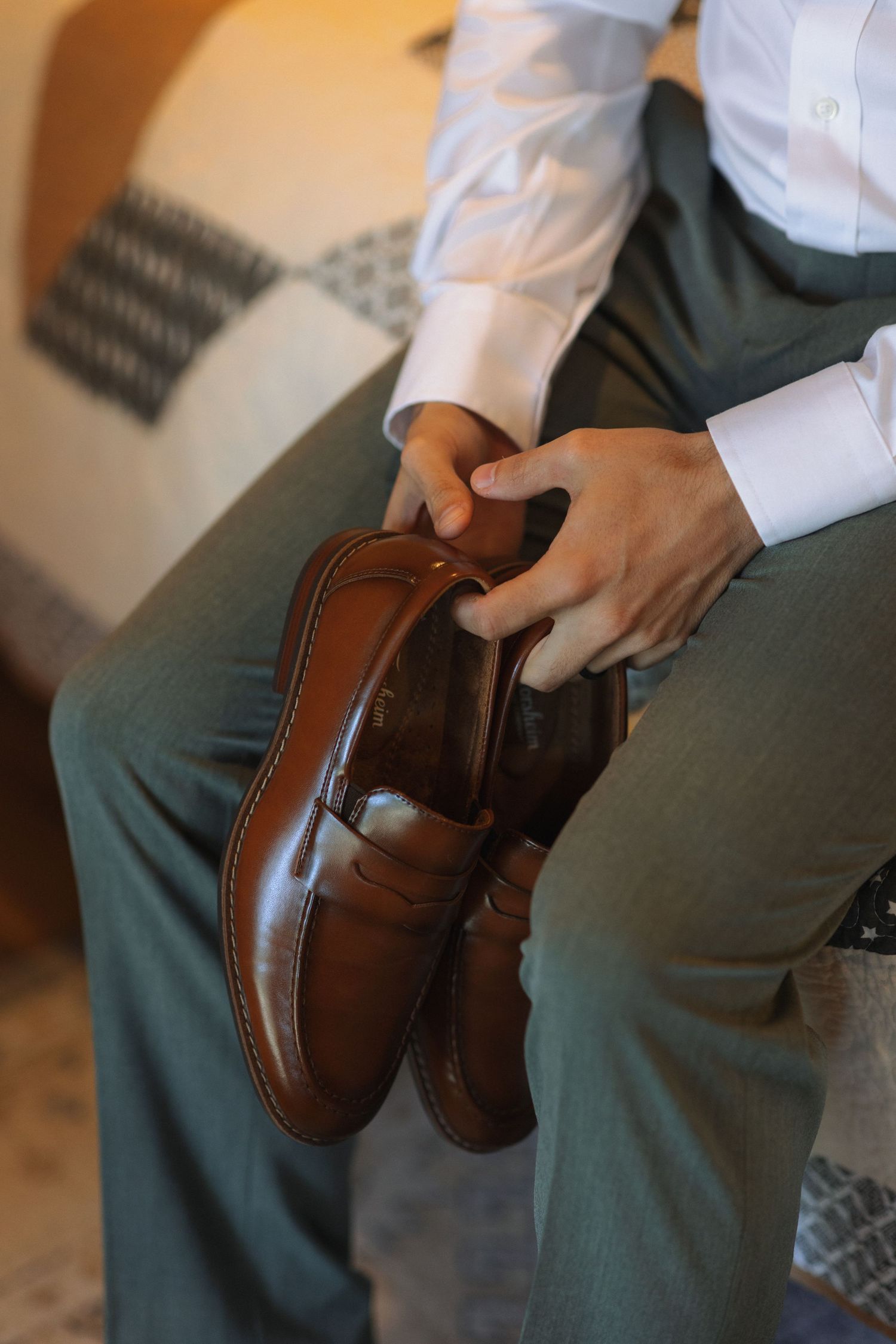 Close-up shots of hands holding and polishing brown leather dress shoes on a gray fabric surface.