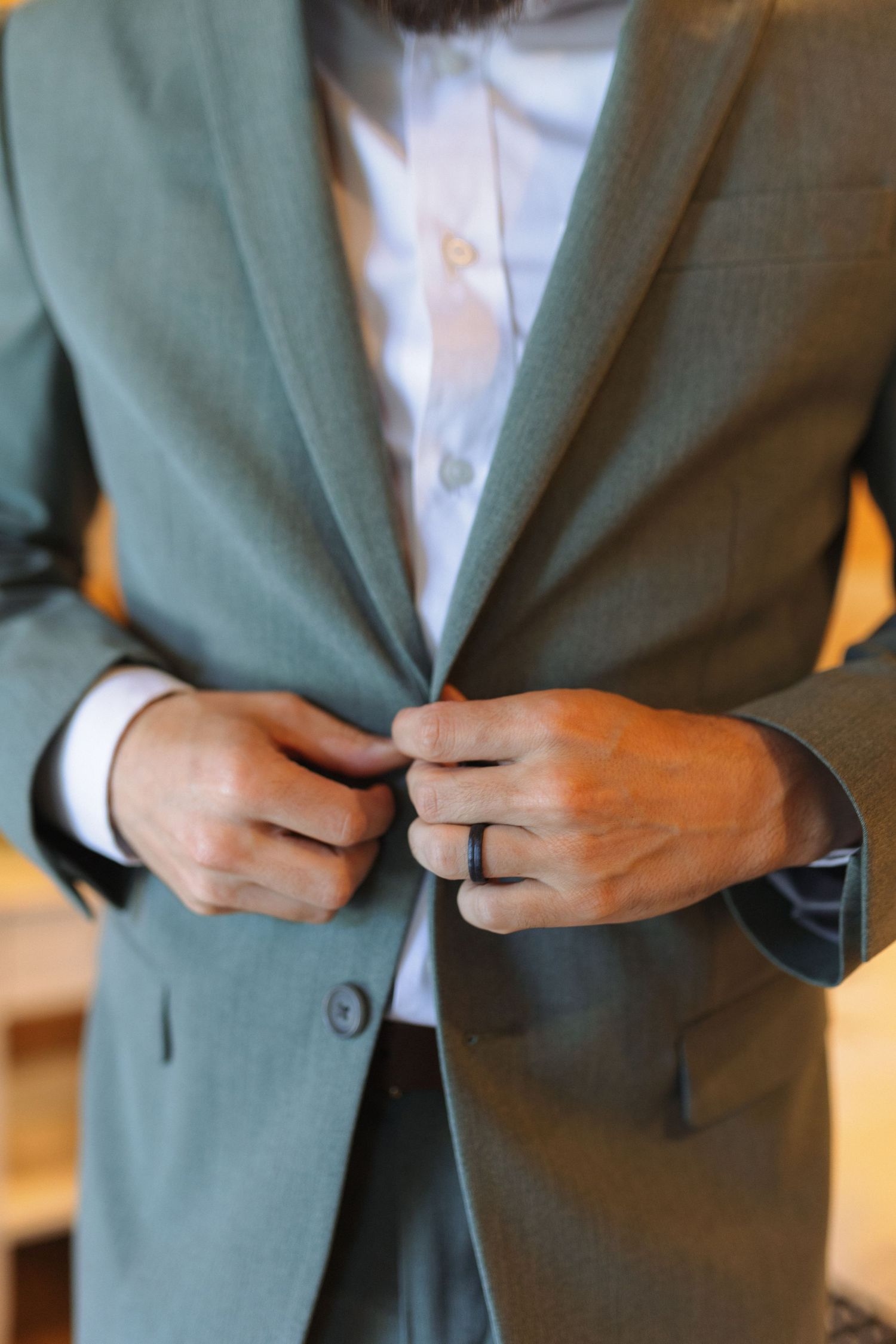 Close-up view of hands fastening buttons on a sage green suit jacket over a white dress shirt.