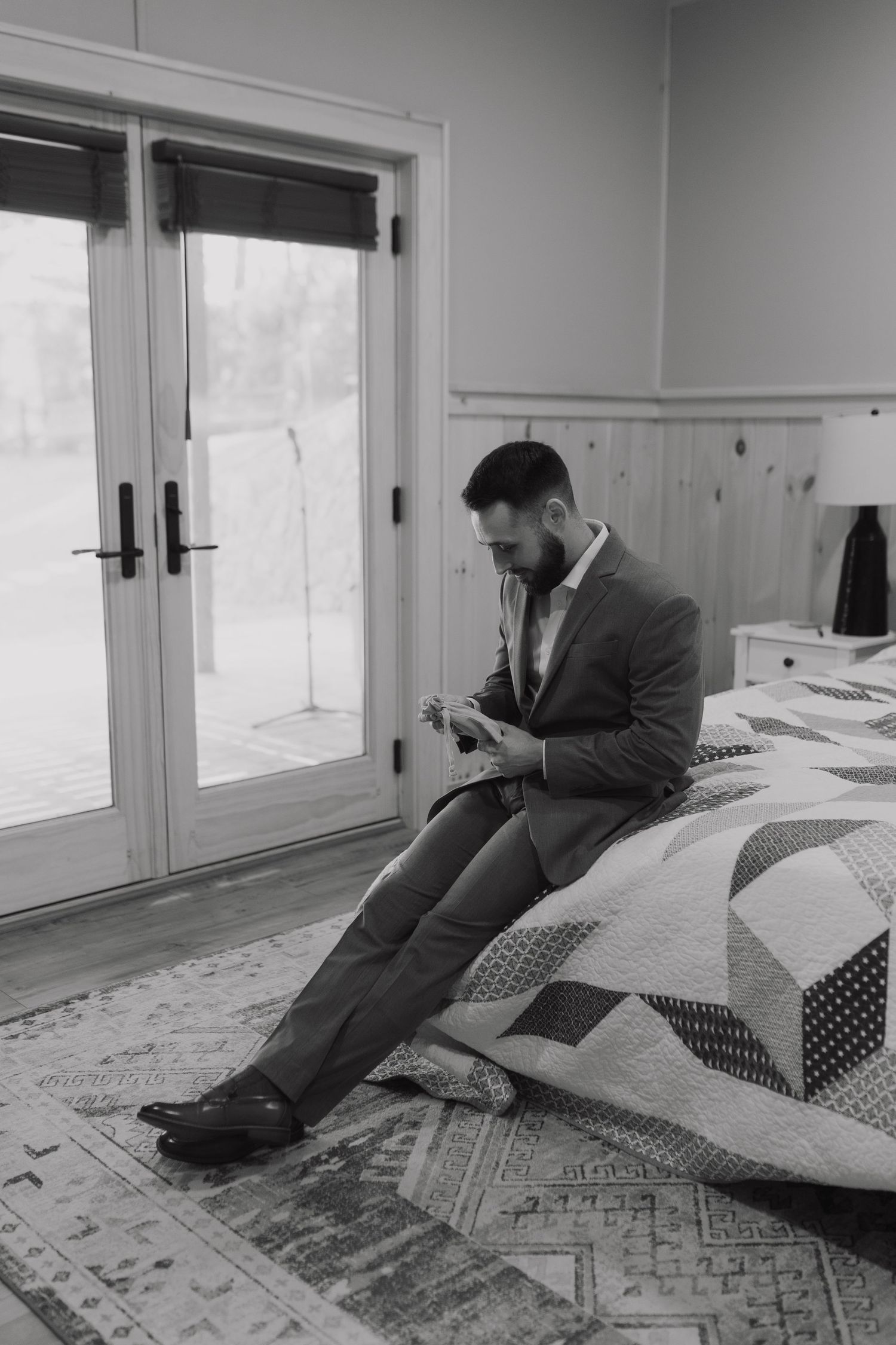 Person in suit lying sideways on a patterned rug near French doors in monochrome photography.
