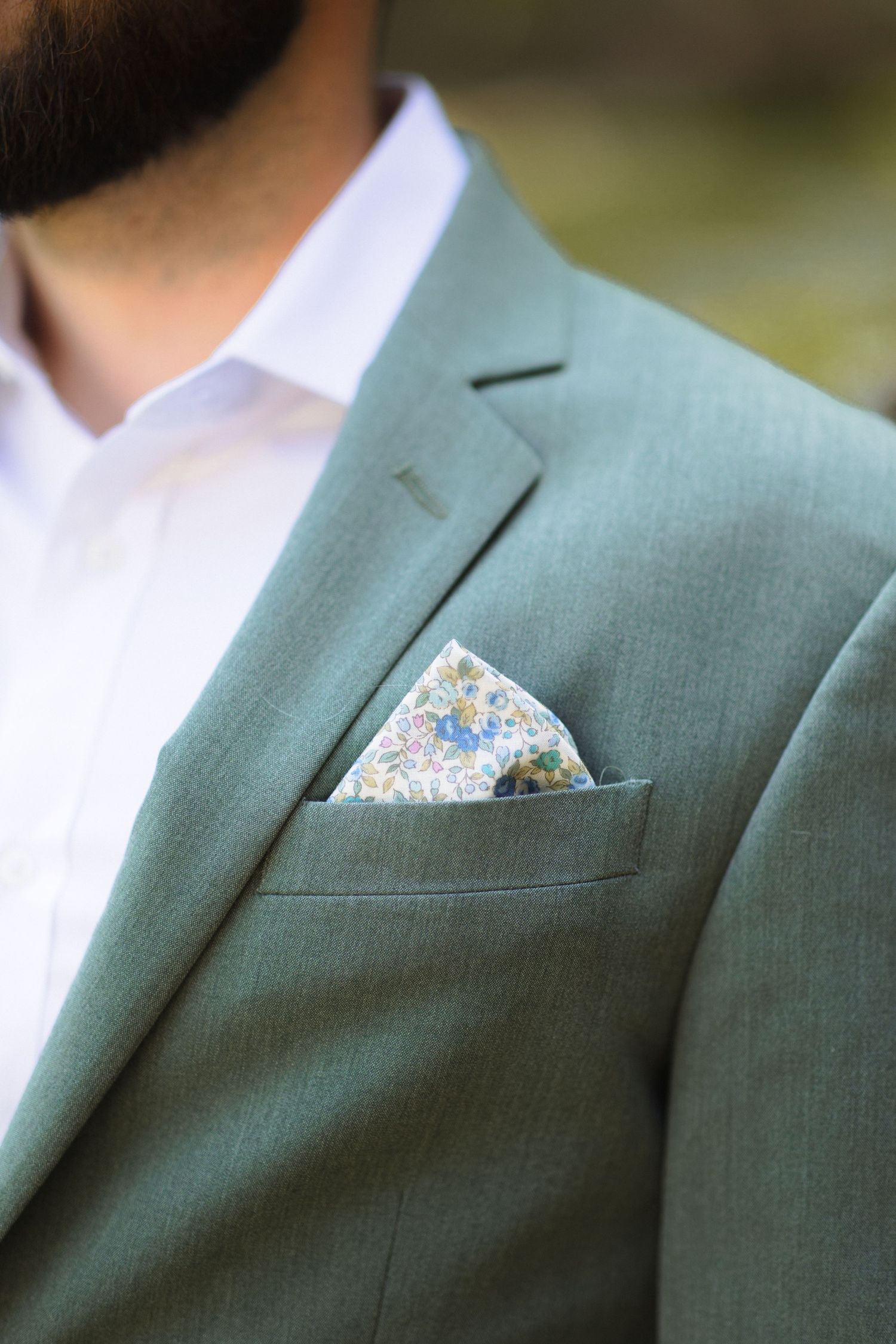 A sage green suit jacket with a floral pocket square in the breast pocket.