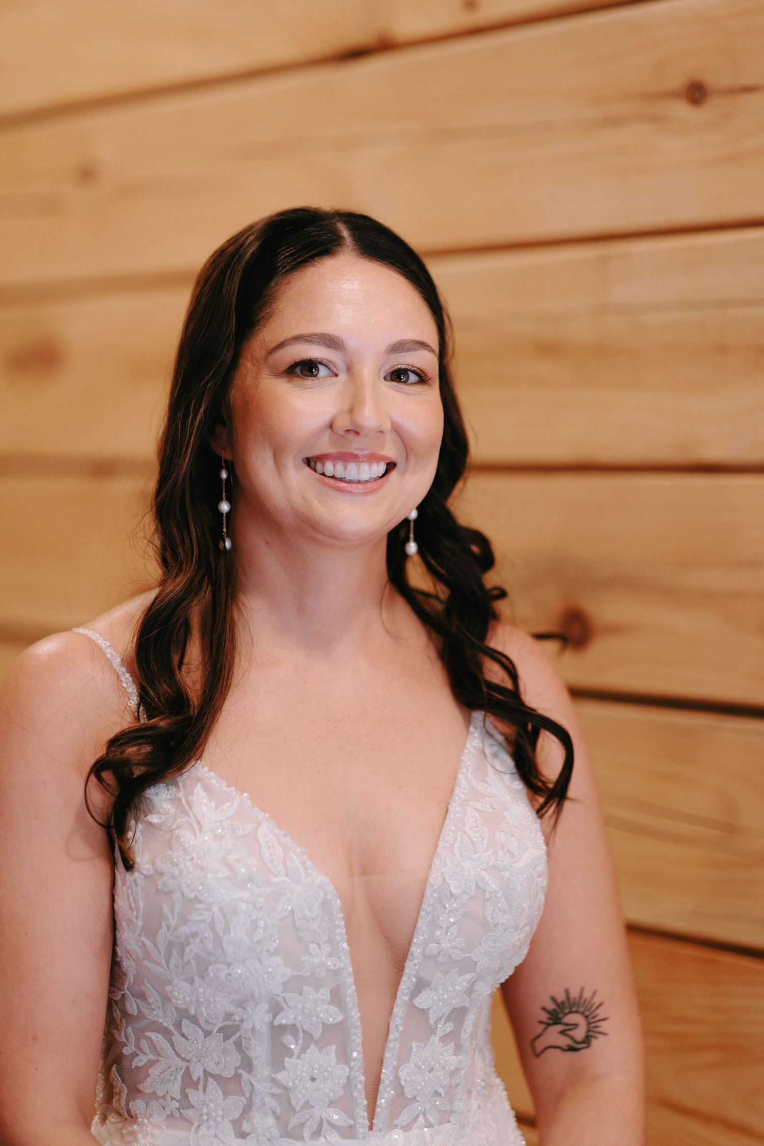 A wedding dress portrait showing delicate lace details and a plunging neckline against wooden wall backdrop.