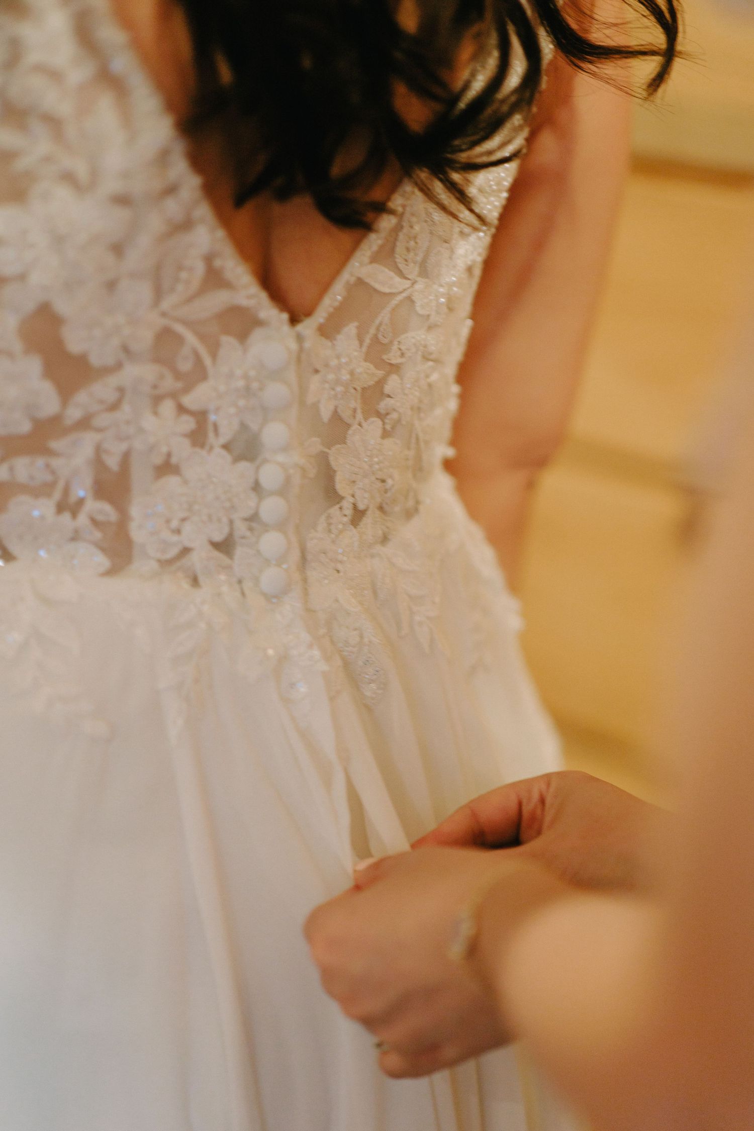 Close-up detail of intricate lace patterns on a white wedding dress with hands adjusting the fabric.