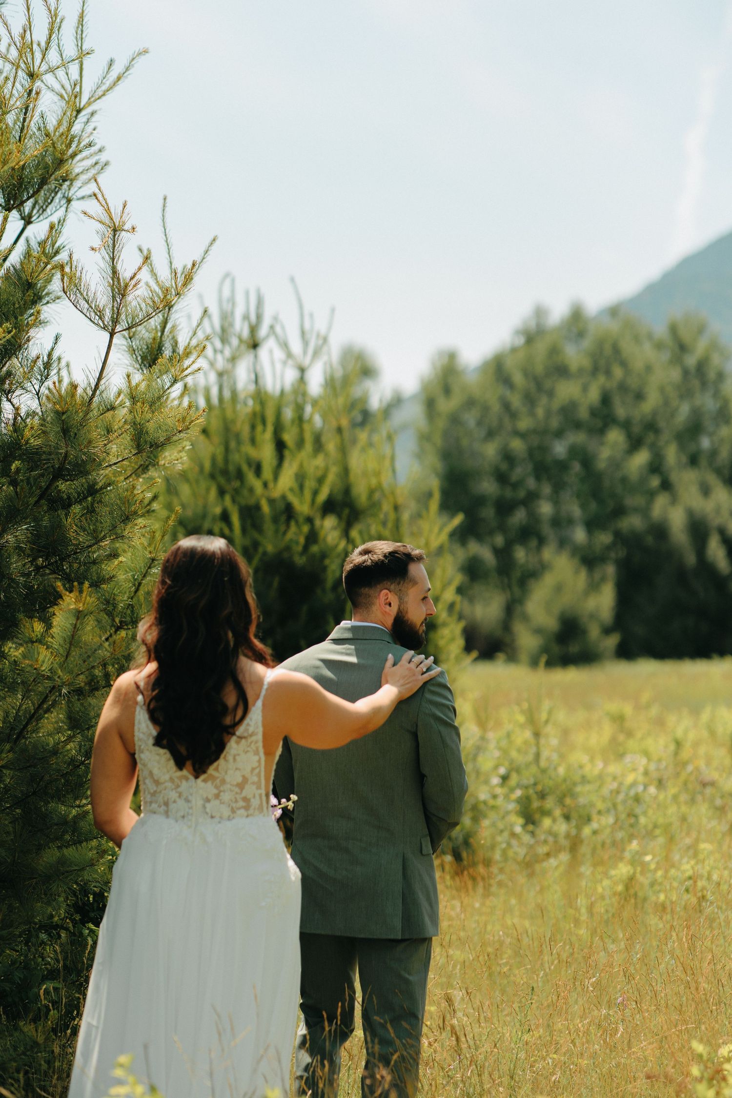 Wedding couple walking together in a sunny meadow with mountains in the distance.