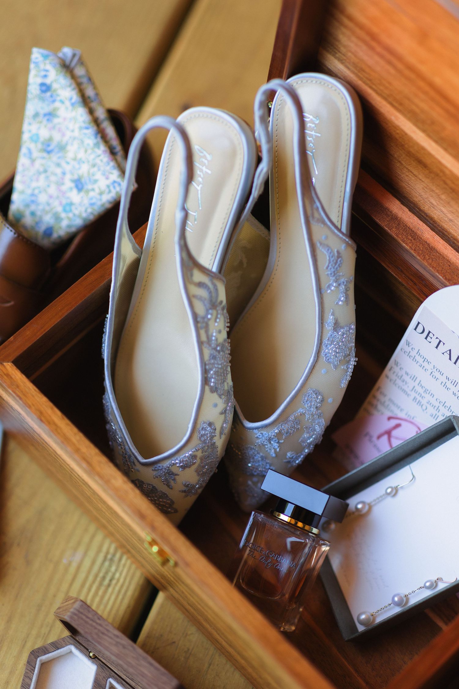 Elegant floral patterned wedding shoes arranged in wooden display boxes.