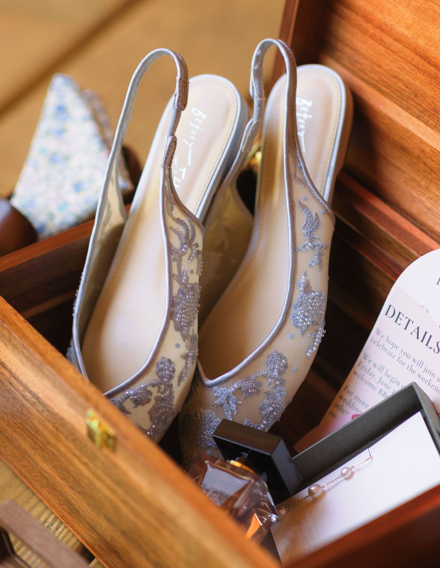 Elegant silver and lace bridal slingback shoes rest in a wooden box with ornate details.