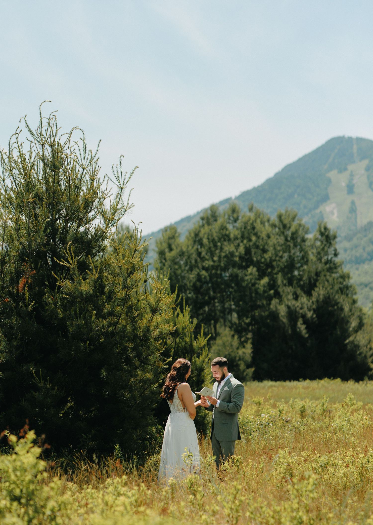 A romantic wedding ceremony takes place in a scenic mountain field surrounded by lush greenery.