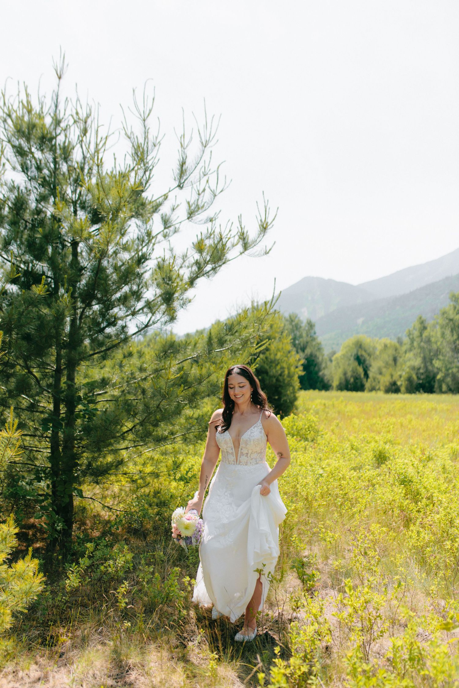 A bride walks gracefully through a sunlit meadow wearing a flowing white dress.