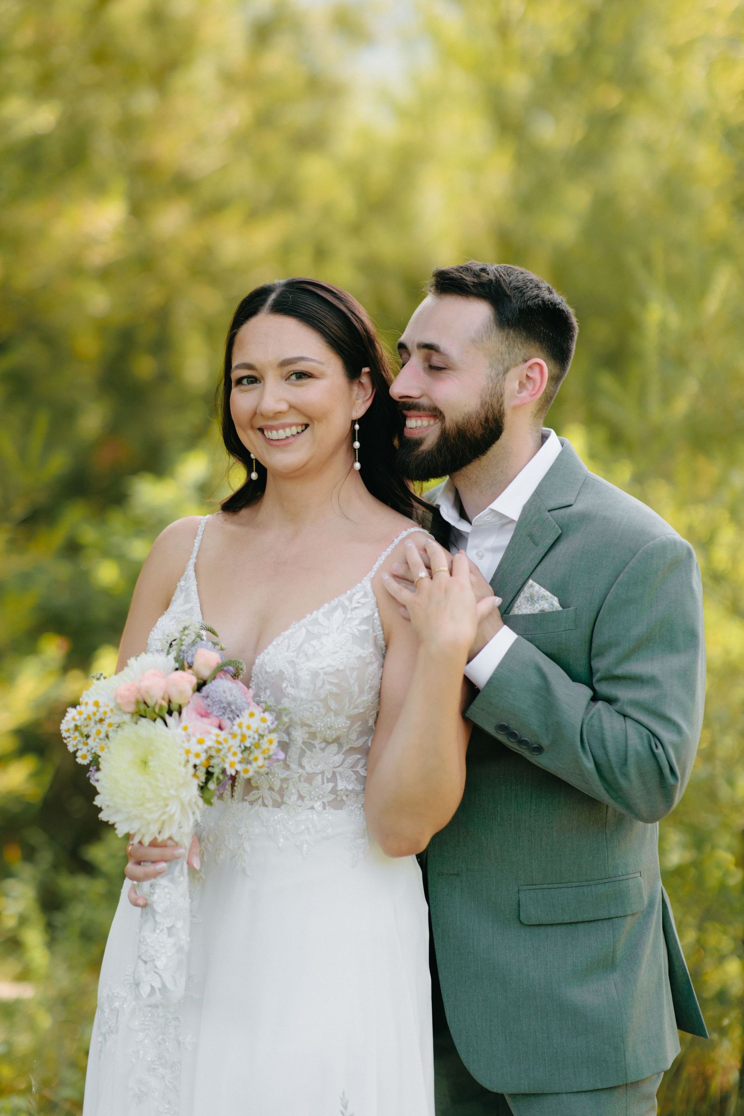 A happy couple shares joyful moments during their wedding photoshoot in a lush outdoor setting.