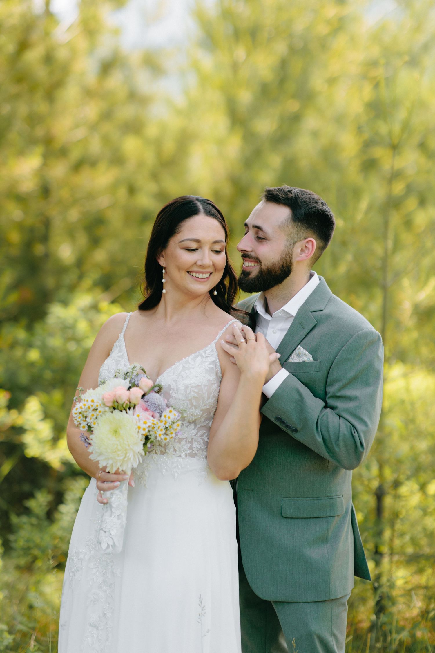 A romantic wedding moment with a couple sharing a tender embrace outdoors with a bouquet of pastel flowers.