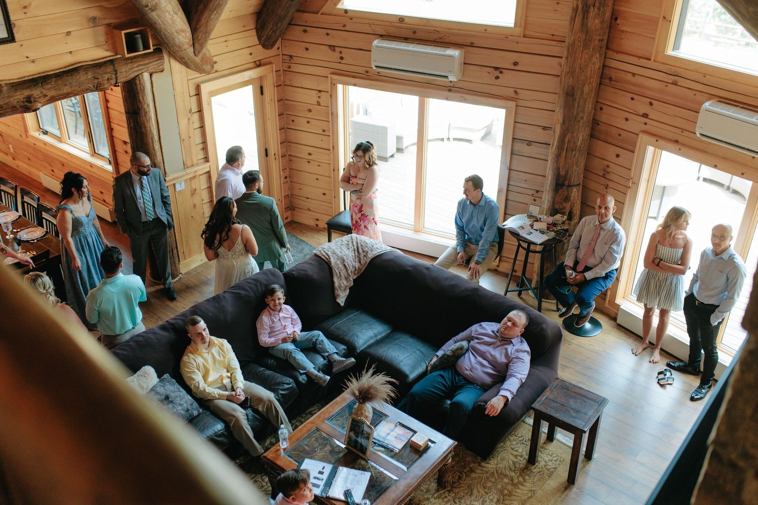 A group of people gathered in a cozy wooden cabin living room with exposed timber walls and large windows.