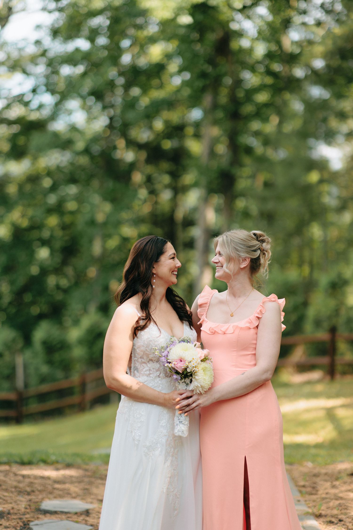Two women share a joyful moment on a forest path while one holds a delicate bouquet.