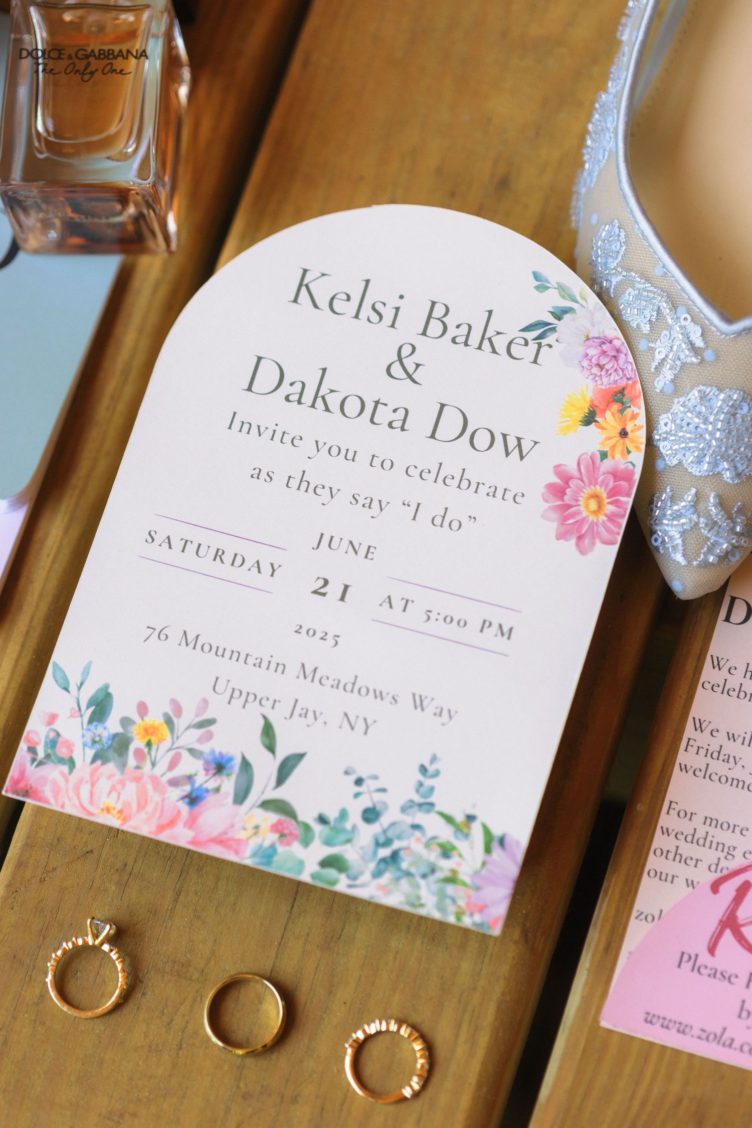 Wedding invitation with floral design and gold rings displayed on wooden surface.