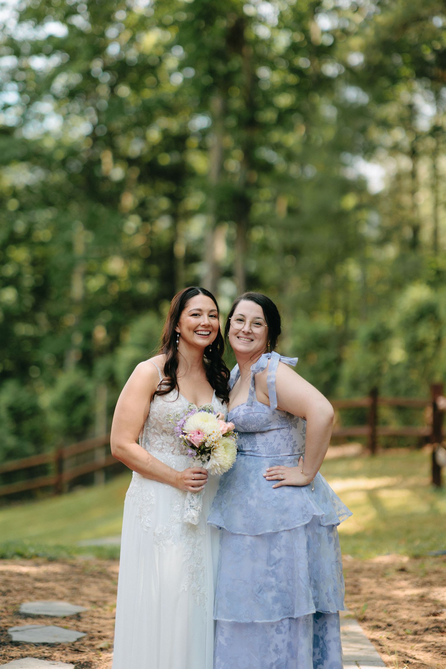 Two wedding attendees in elegant dresses share a joyful moment together on a wooden deck.