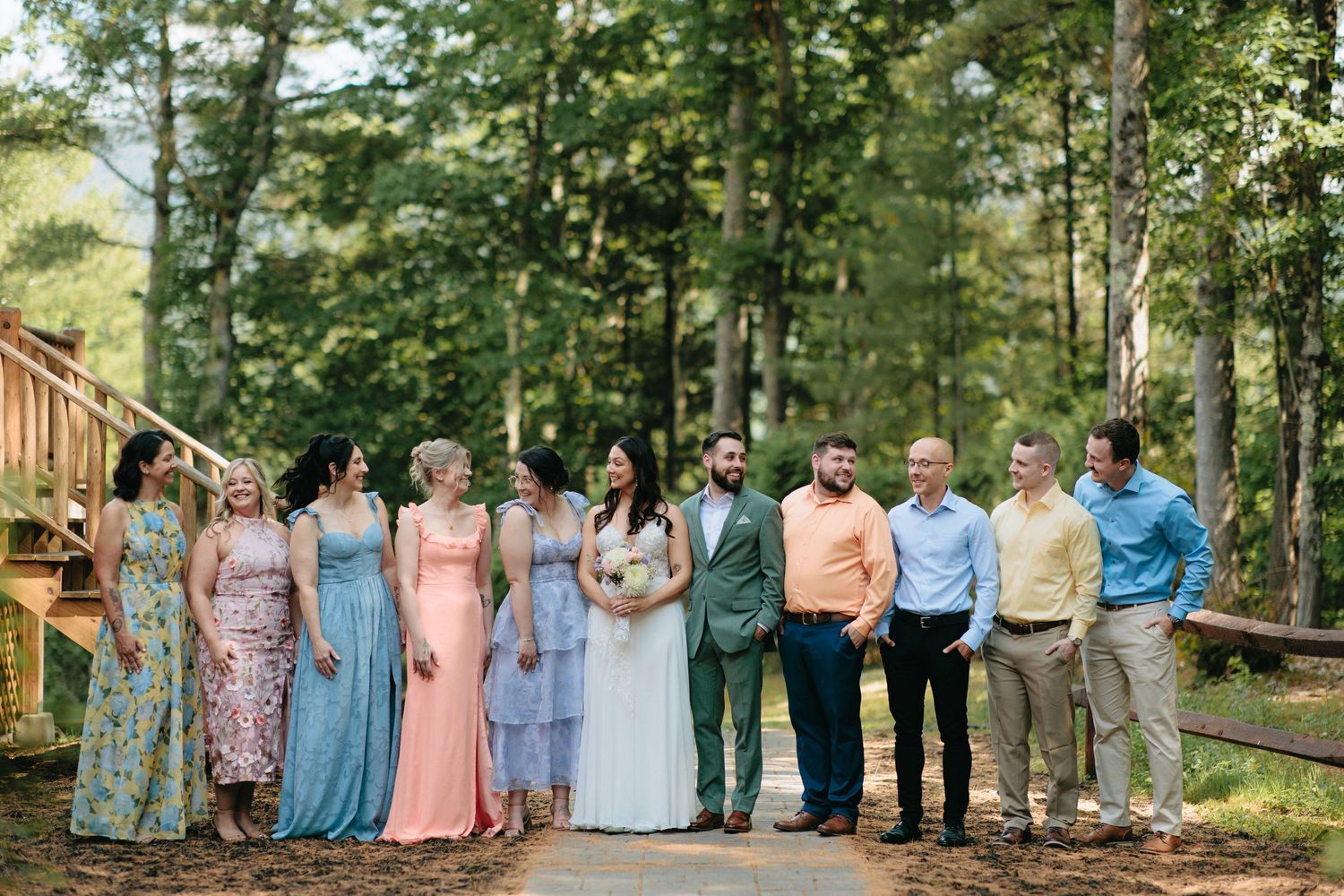 Wedding party lined up in pastel dresses and formal attire for outdoor group photos.
