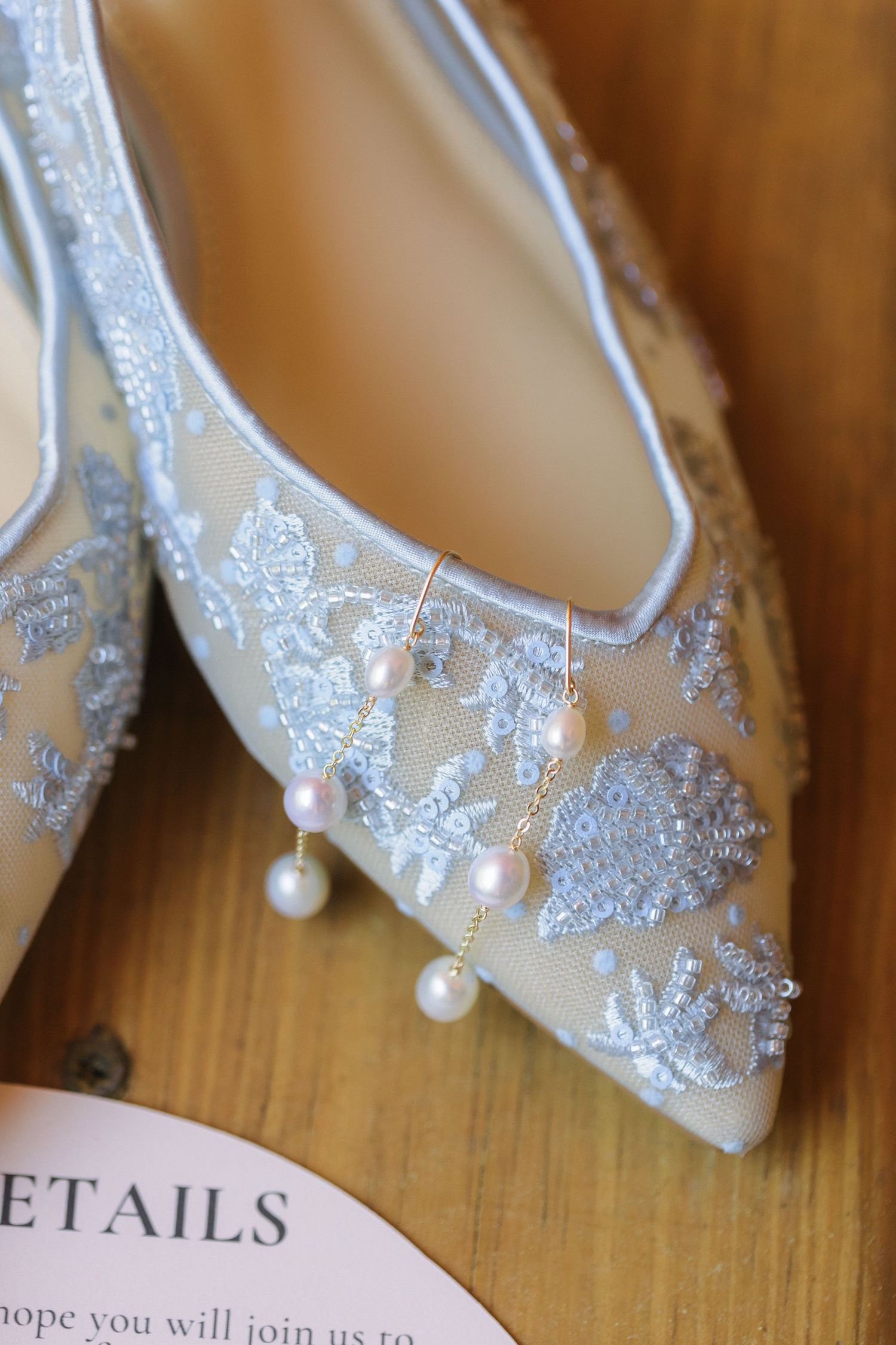 Detailed shot of silver lace bridal flats decorated with delicate pearl embellishments.