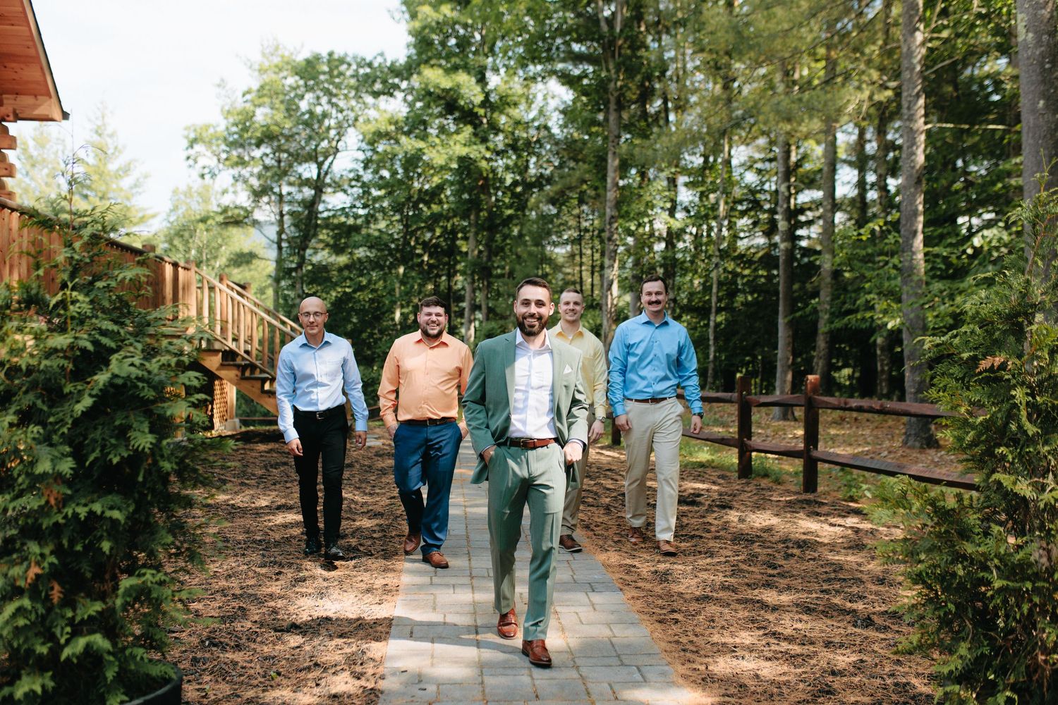 A group of people walking together on a wooded path surrounded by tall green trees and pine needles on the ground.