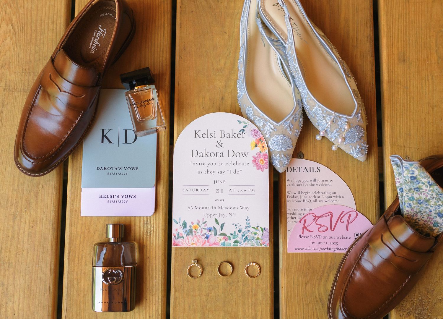 Wedding details flatlay featuring brown leather shoes, floral invitations, and wedding rings on wooden surface.