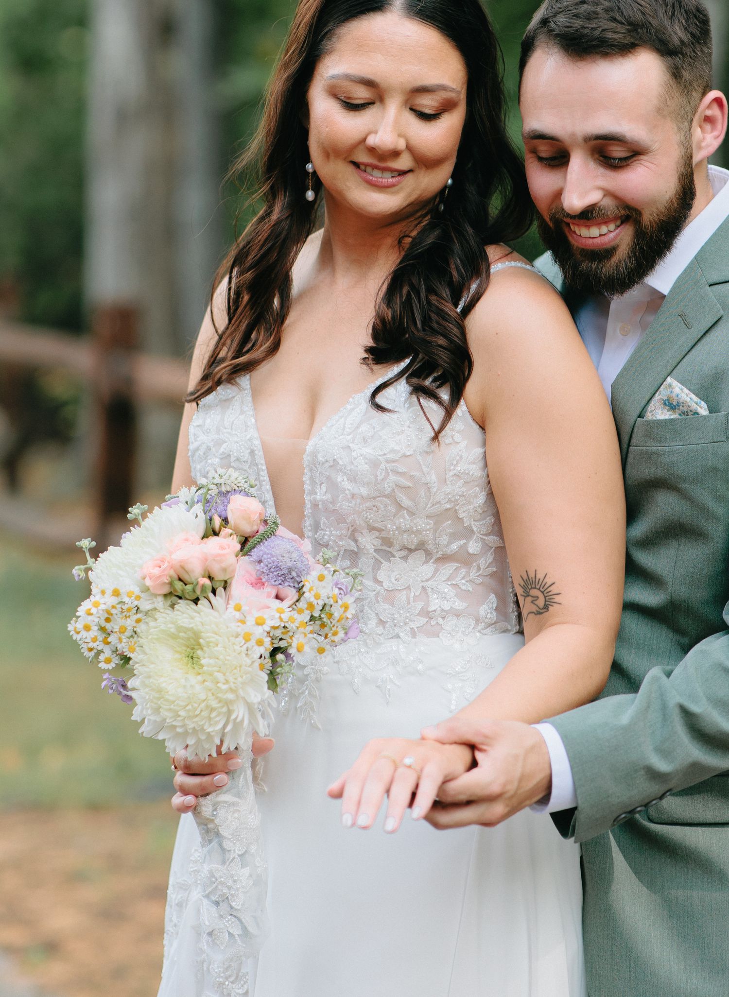 A tender wedding photograph showing a couple embracing while admiring a soft pastel bouquet.