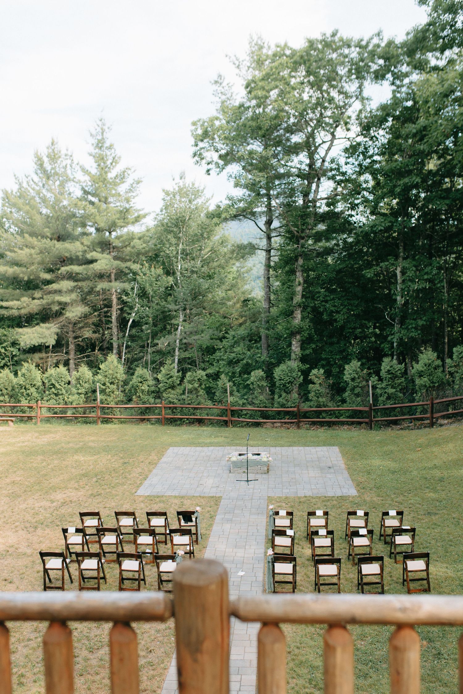 Outdoor wedding ceremony setup with wooden chairs facing a stone patio surrounded by lush forest trees.