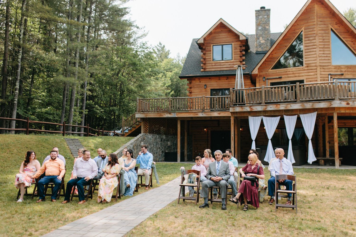 Wedding guests seated outside a rustic log cabin during an outdoor ceremony.