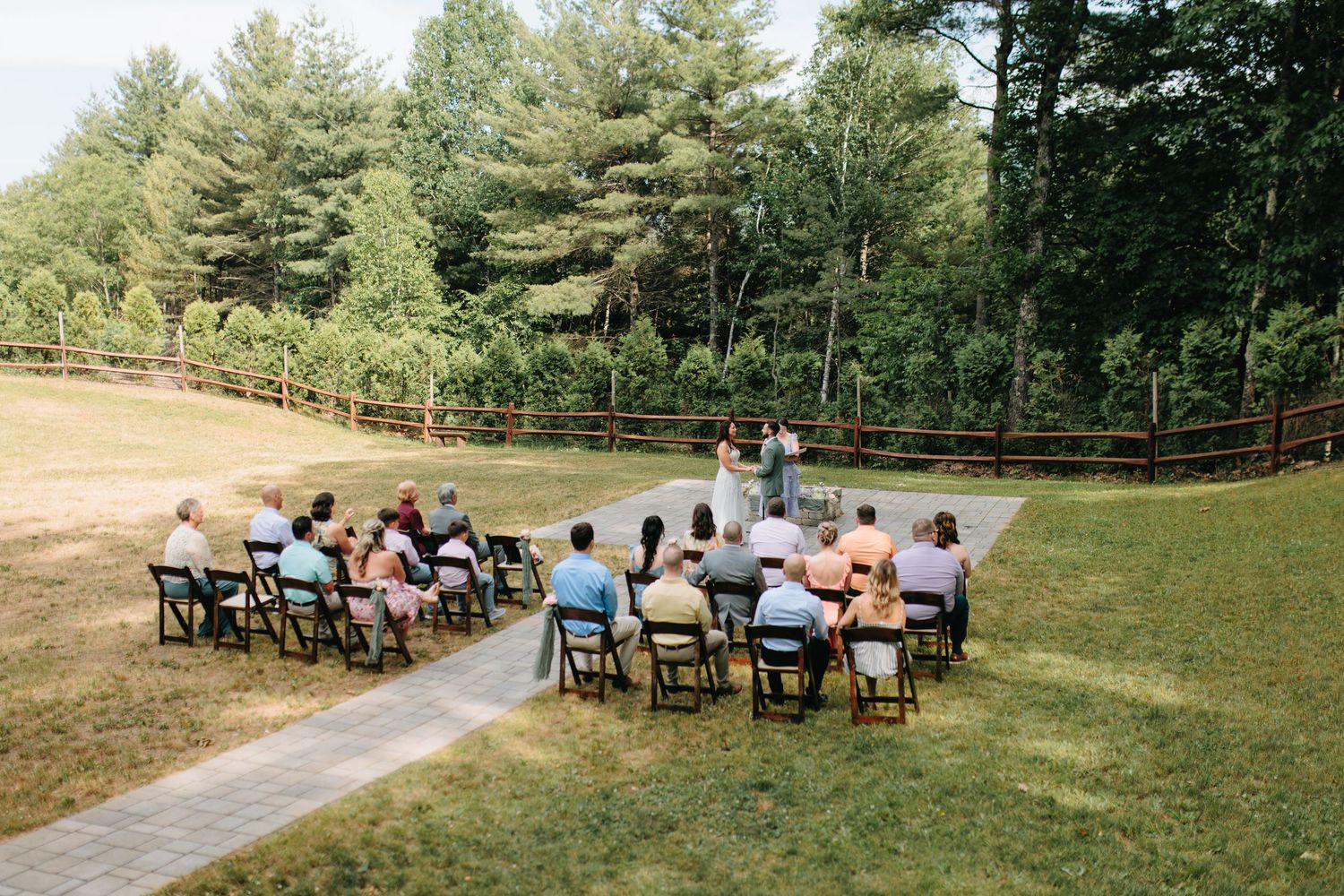 Wide panoramic view of an outdoor wedding ceremony setup with wooden chairs in a forested area.