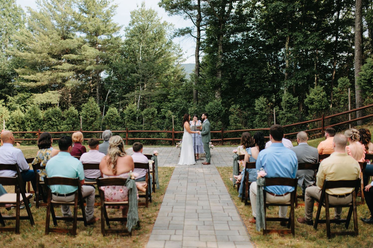 Outdoor wedding ceremony seating arrangement with wooden chairs along a stone pathway near a log cabin.