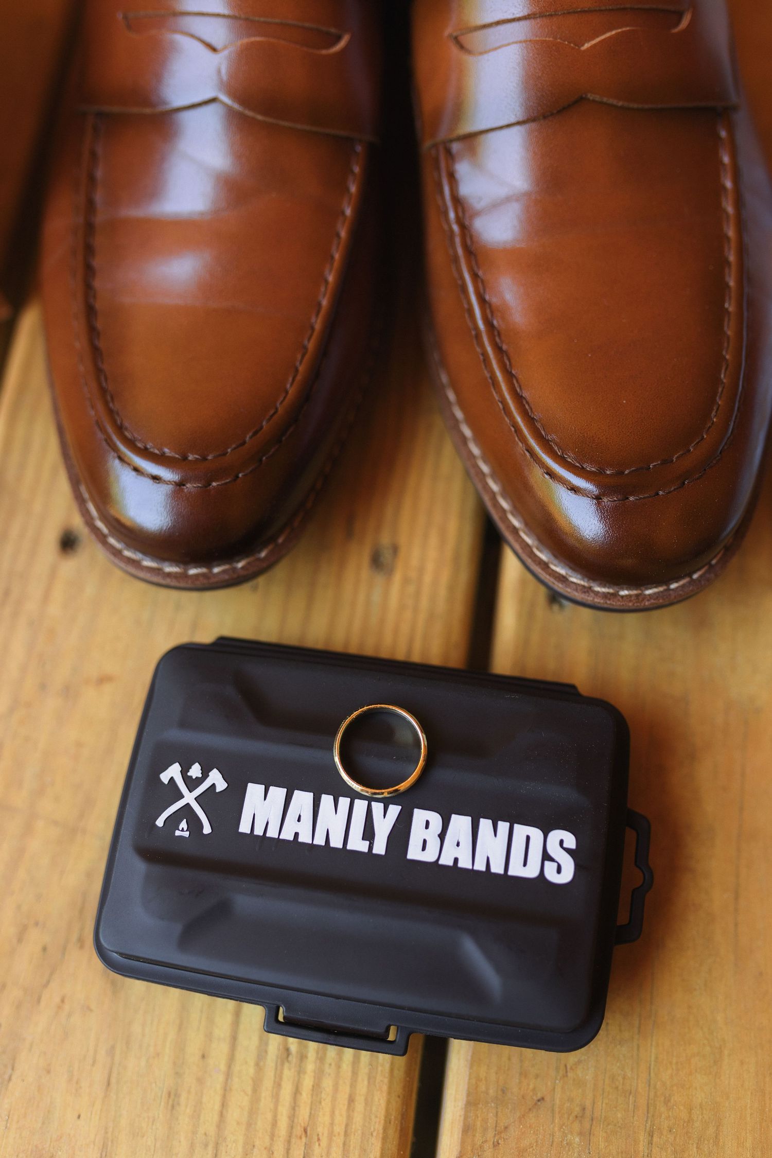 Close-up of brown leather loafers with a black Manly Bands box on wooden surface.