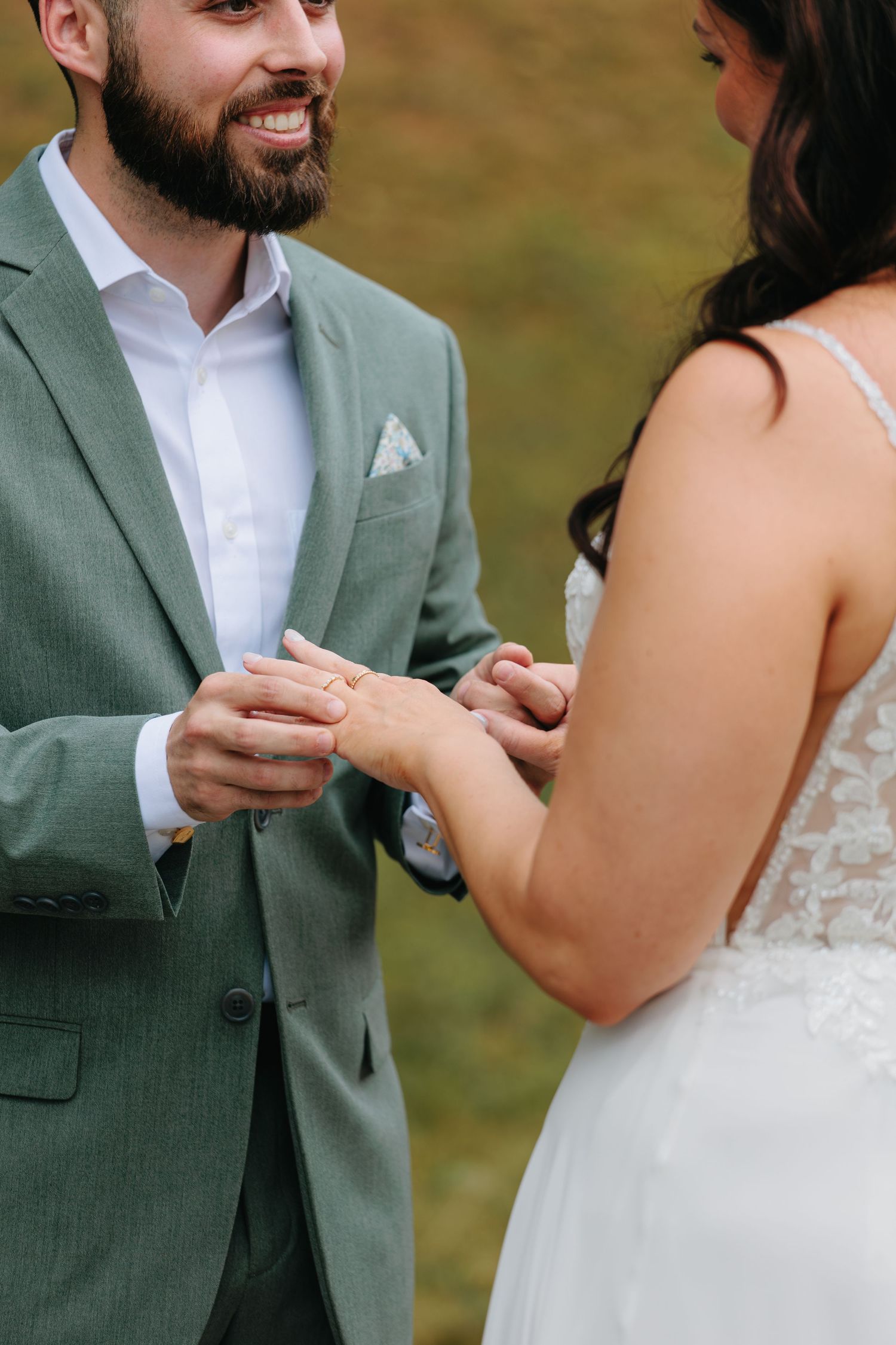 Close-up shot of hands exchanging rings during an outdoor wedding ceremony.