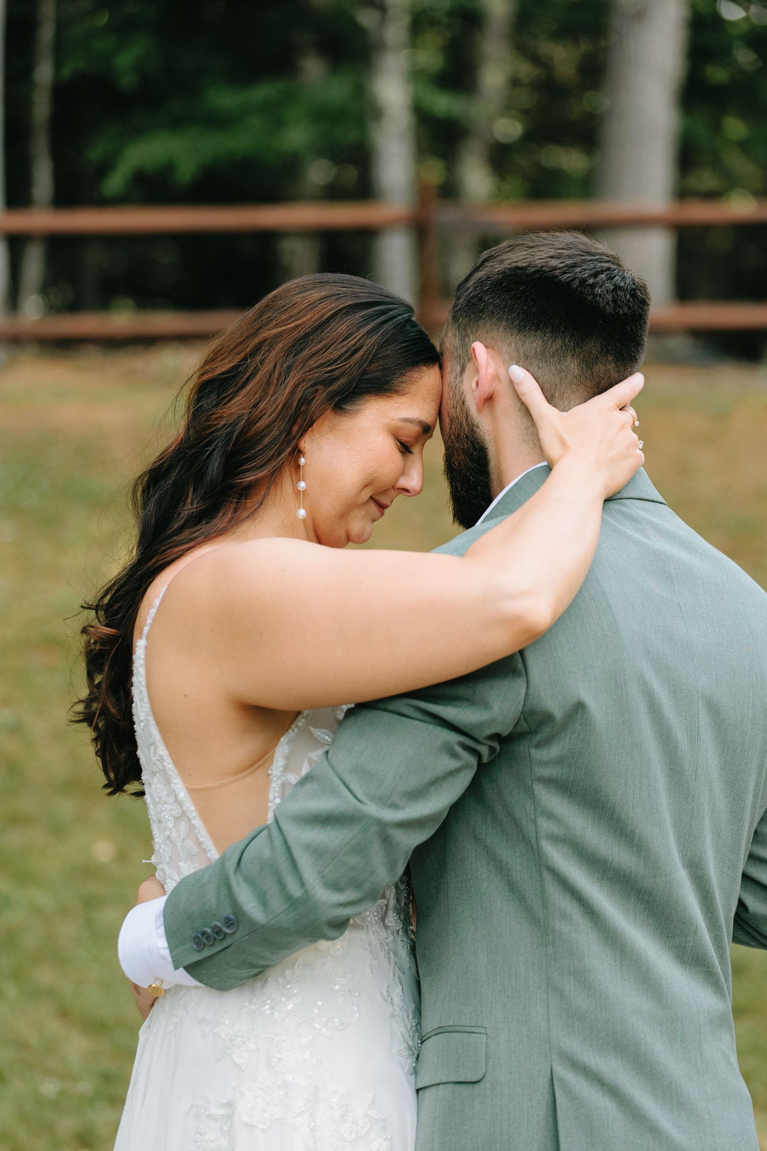 A tender moment between newlyweds as they share an intimate embrace outdoors, the bride in white and groom in sage green.