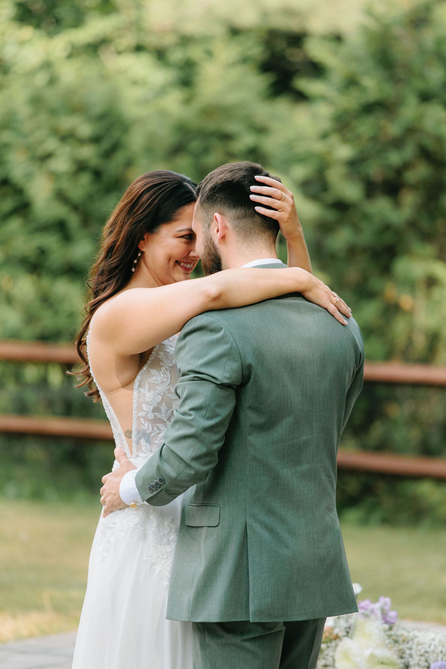 A couple embraces tenderly during their wedding photos in a green garden setting.
