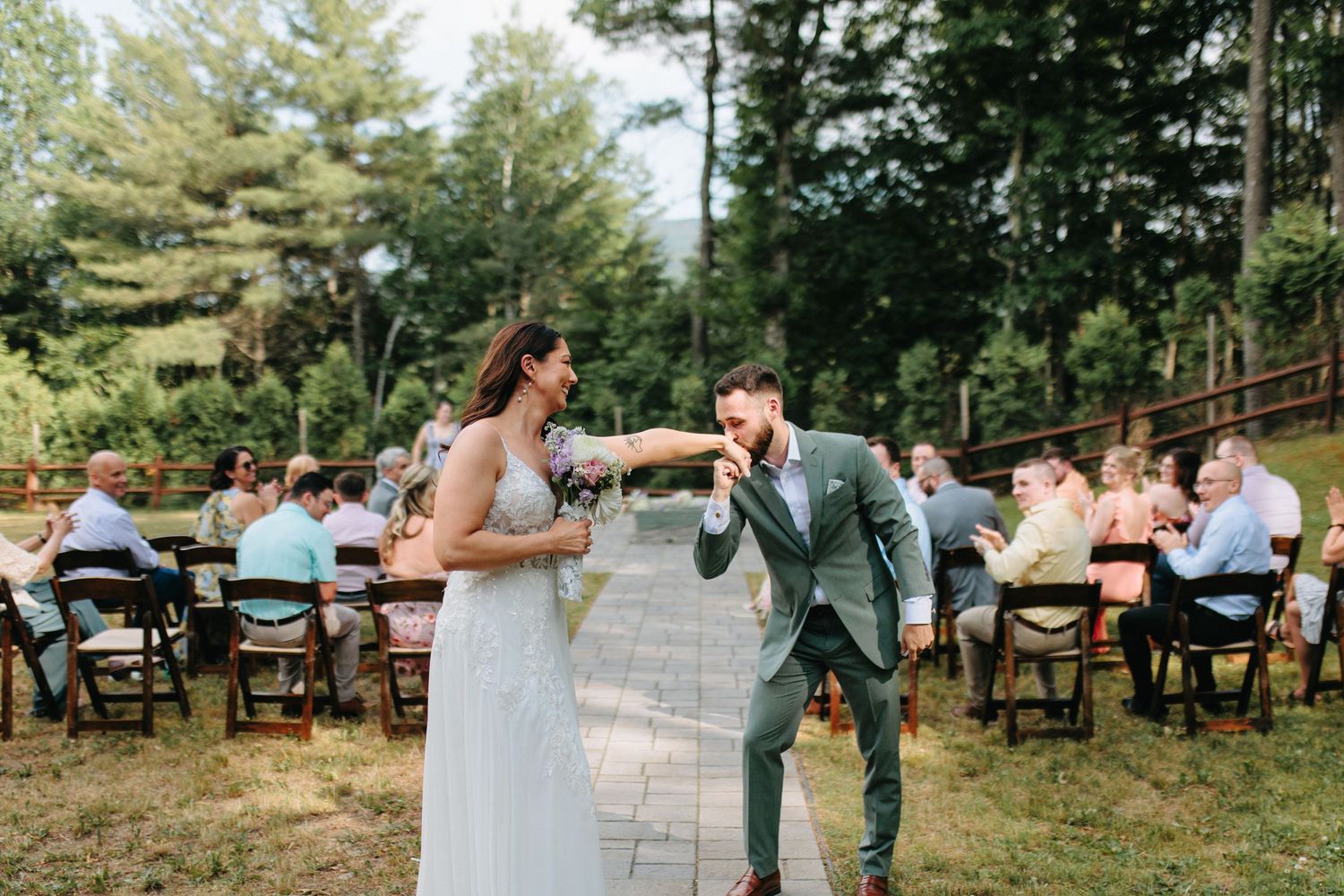 Wedding guests gather for an intimate outdoor ceremony surrounded by tall pine trees.