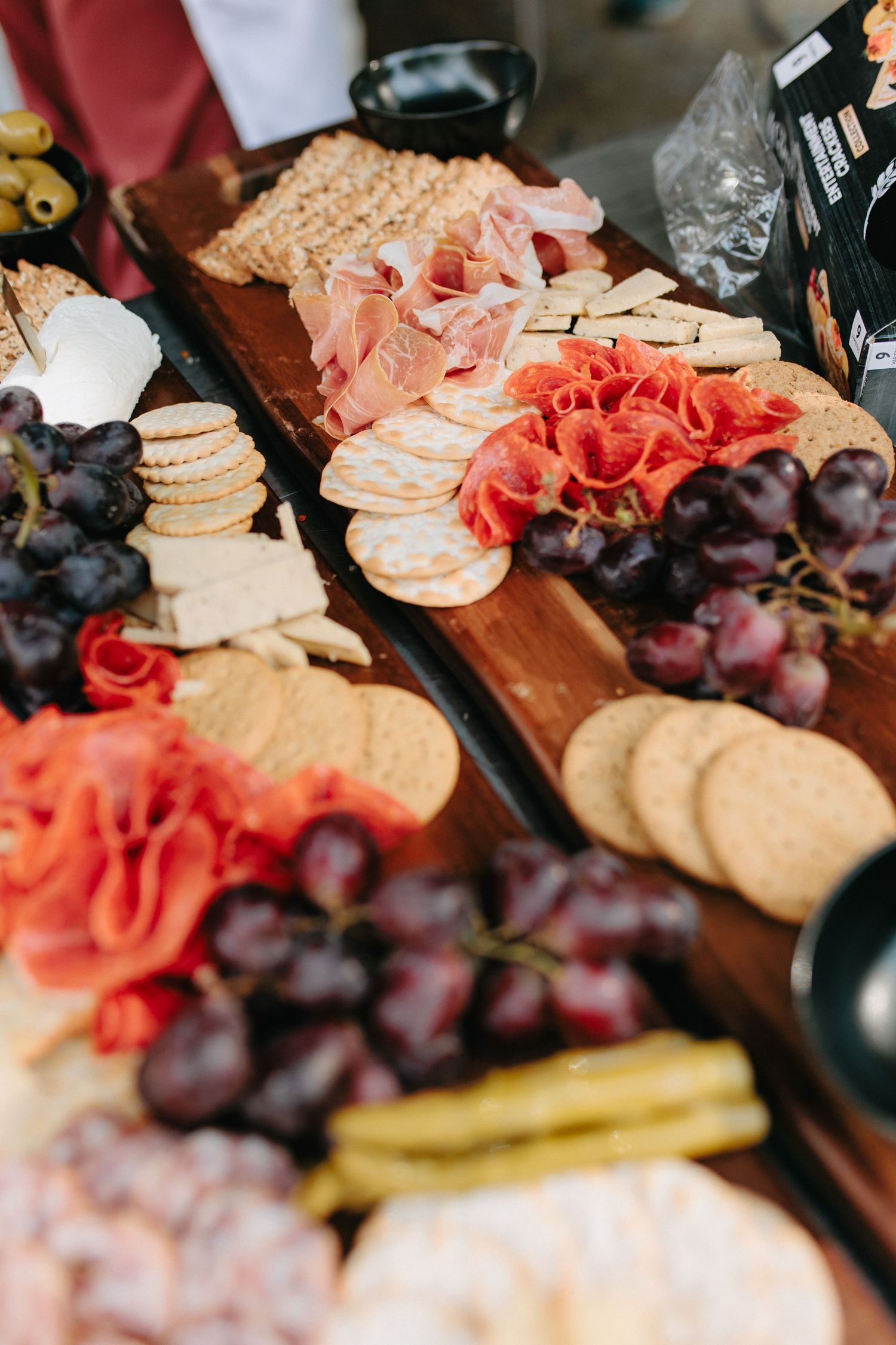 Close-up view of an elegant charcuterie board with fresh flowers, cheeses, crackers, and purple grapes.