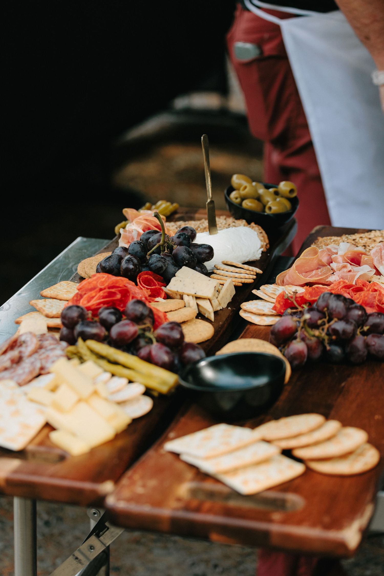 A charcuterie board with cheese, crackers, grapes, and garnishes arranged on a wooden serving platter.