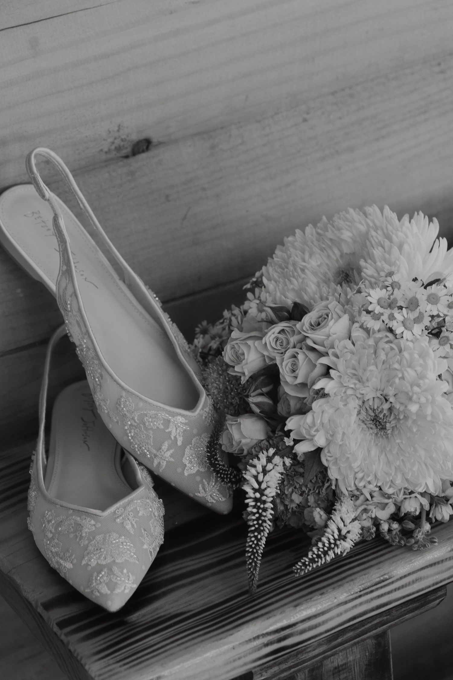 Vintage lace bridal shoes next to white floral bouquet in black and white photography.
