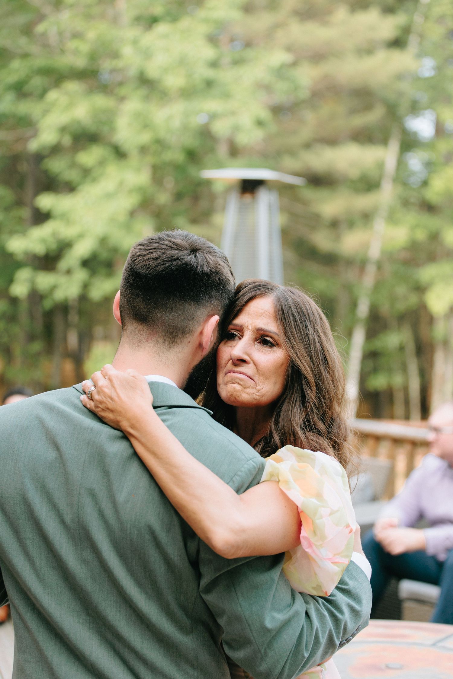 A couple shares a tender moment embracing outdoors with green foliage in the background.