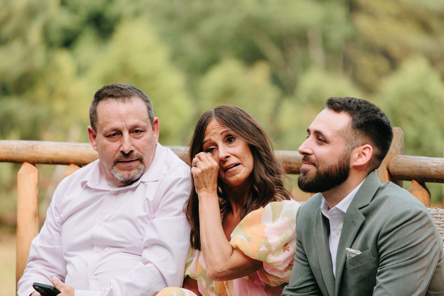 Three people sitting together on outdoor wooden bench laughing and enjoying a lighthearted moment.