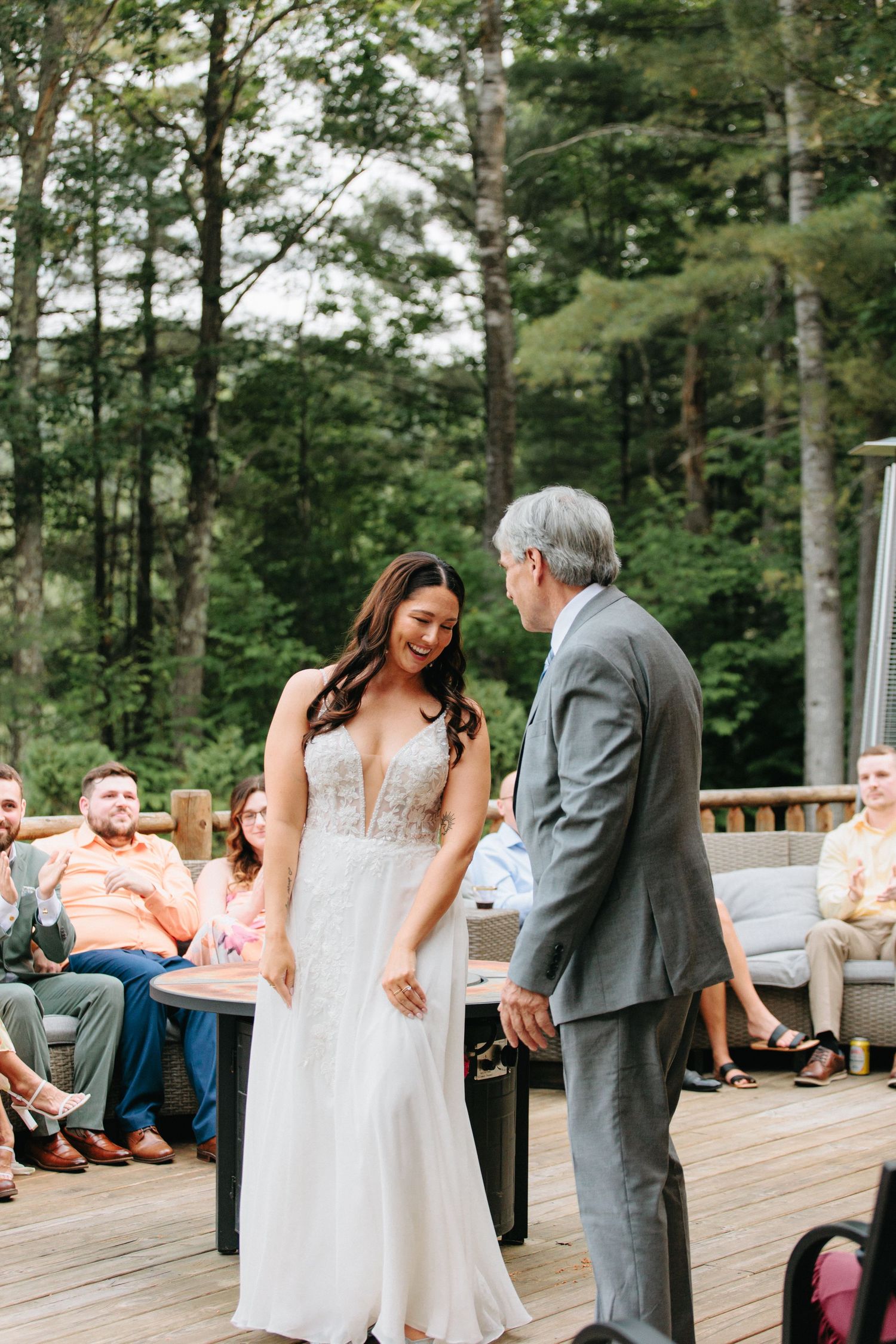 A couple shares an emotional moment during their outdoor wedding ceremony on a wooden deck surrounded by trees.