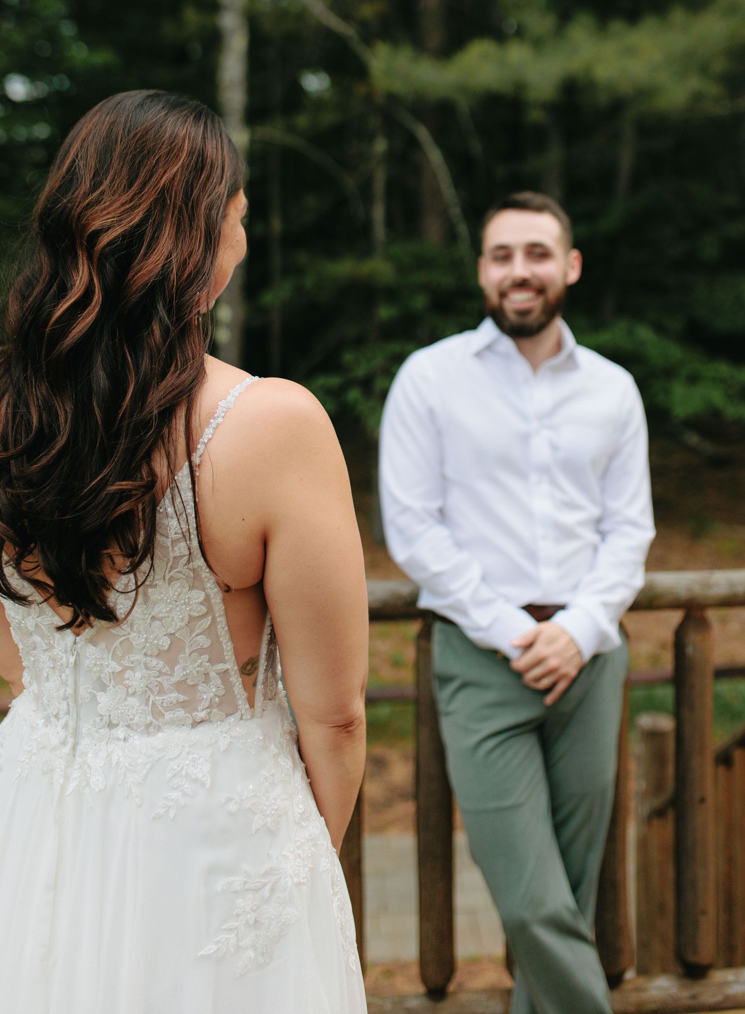 A couple shares a first look moment on their wedding day as they stand on a wooden deck surrounded by trees.