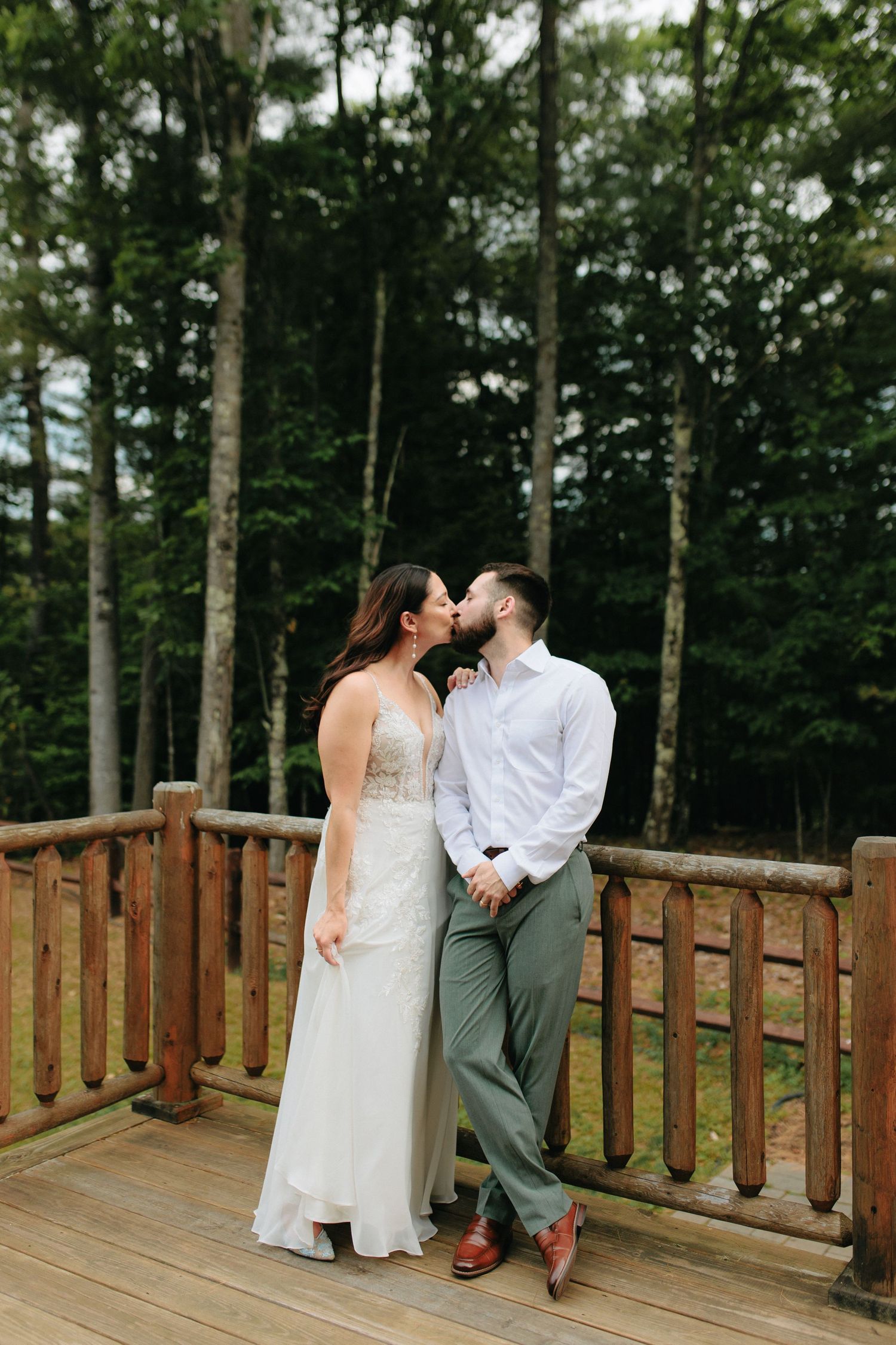 A couple embraces on a wooden deck overlooking a forest during an intimate wedding ceremony.