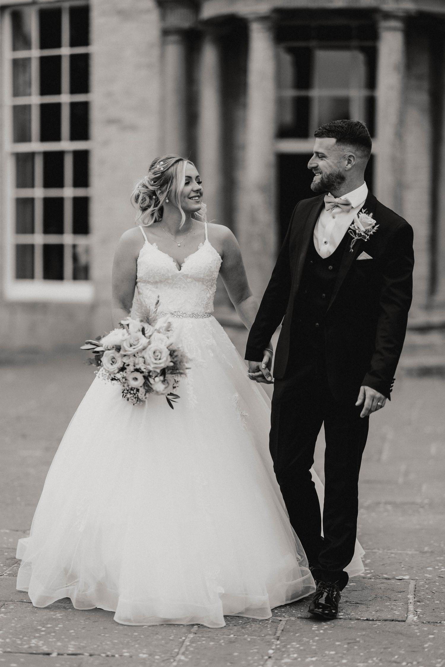 Bridesmaids in light gray dresses hold white and blush pink floral bouquets at an elegant wedding ceremony.