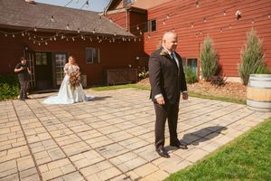 Wedding couple takes romantic photos on stone patio outside rustic red barn venue during sunset.
