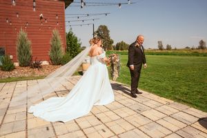 Wedding photography session with elegant white dress train laid out on stone patio near red barn.