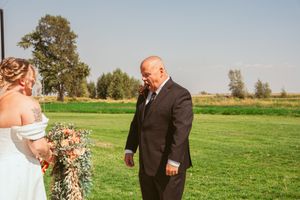 An outdoor wedding ceremony on a sunny day in a green field with trees in the background.