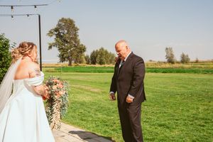 Two people share a special moment during a wedding ceremony on a sunny day at an outdoor venue with string lights overhead.
