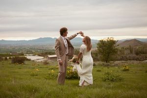 A couple dances together on a hilltop overlooking a scenic mountain landscape at sunset.