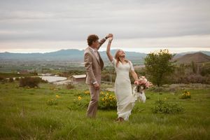 A joyful couple dances on a hilltop meadow at sunset with mountain views in the background.