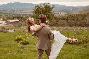 A couple celebrates their wedding day with a joyful embrace on a hilltop overlooking a scenic mountain landscape.