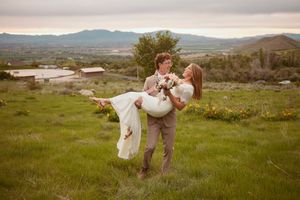 A couple shares a romantic moment in a grassy meadow with rolling hills and mountains in the background.